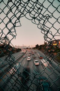 chain link fence with hole showing a road with cars